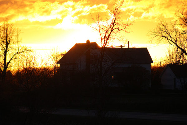 farmhouse silhouetted in front of a blazing sunset