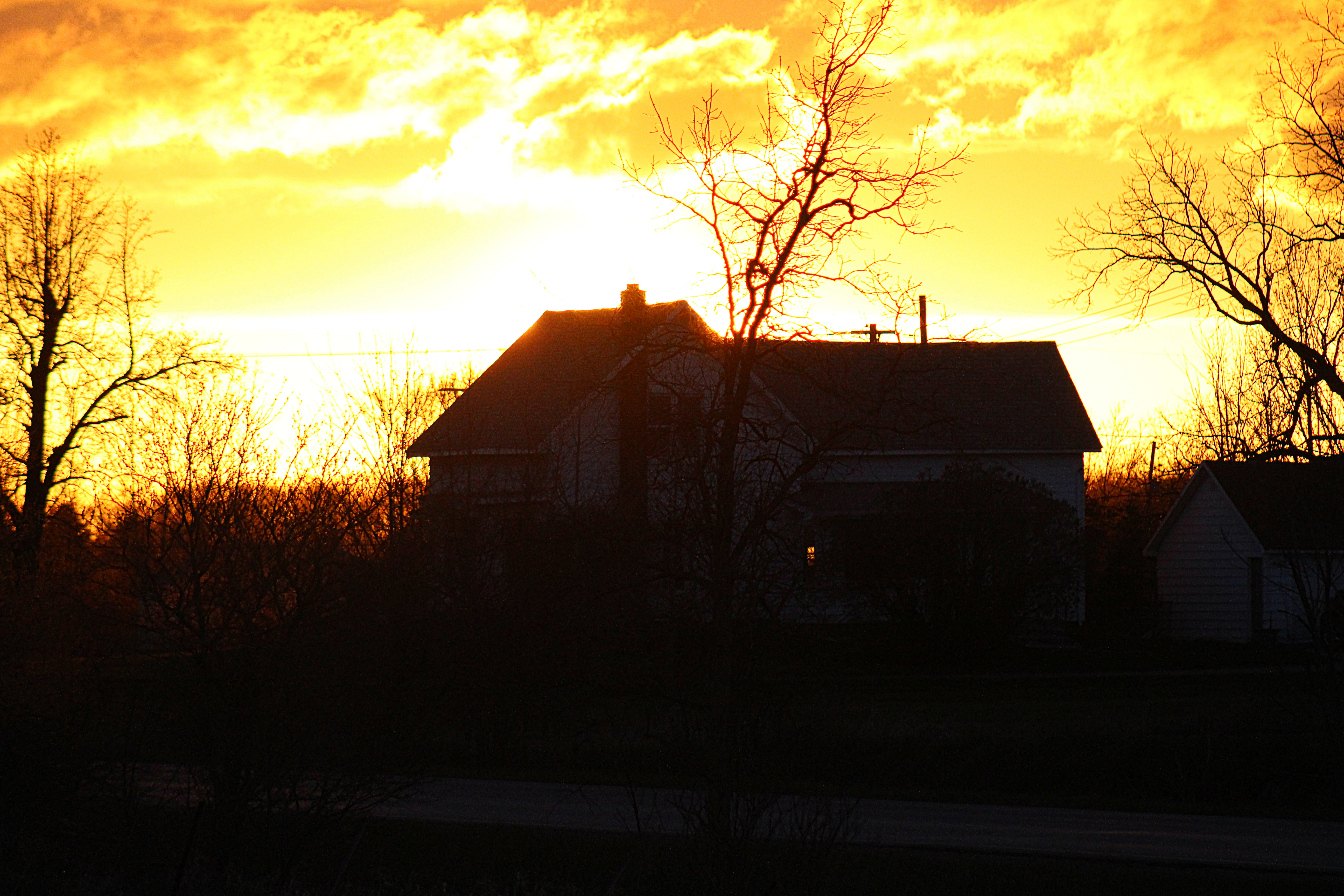 farmhouse silhouetted in front of a blazing sunset