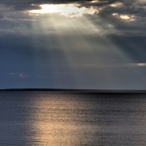 morning sun shining through hole in clouds reflecting glow on lake huron
