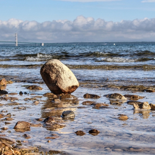 large boulder sitting on lake huron shore tilted at an angle with mackinac bridge in background