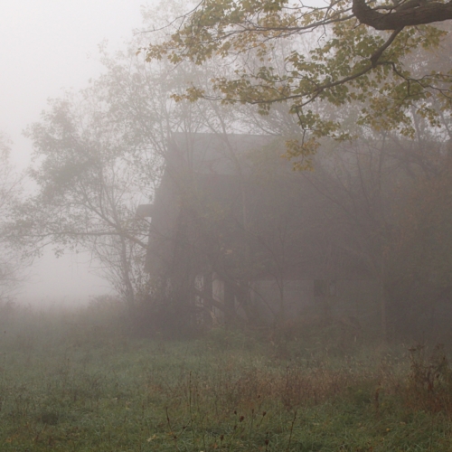 old abandoned barn sits in empty field with fog all around it