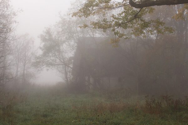 old abandoned barn sits in empty field with fog all around it