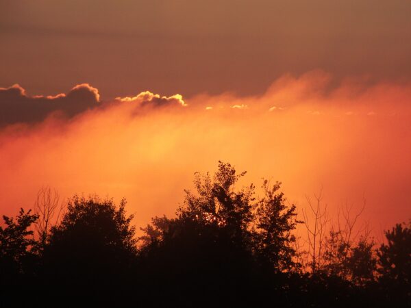 the sky looks like it's on fire from the blazing sun through the hazy clouds at sunset