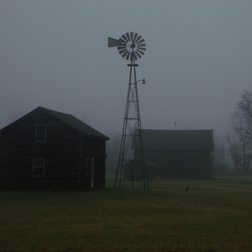 old buildings sit by a windmill on foggy morning