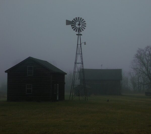 old buildings sit by a windmill on foggy morning