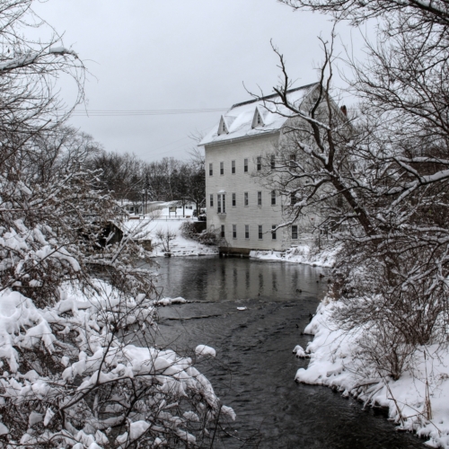 old mill building sits on mill pond surrounded by snow